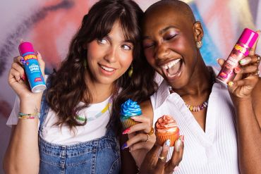 Two women happily holding cupcakes and colorful spray cans.