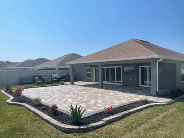 Modern backyard patio with tiled flooring and garden beds under clear blue sky.