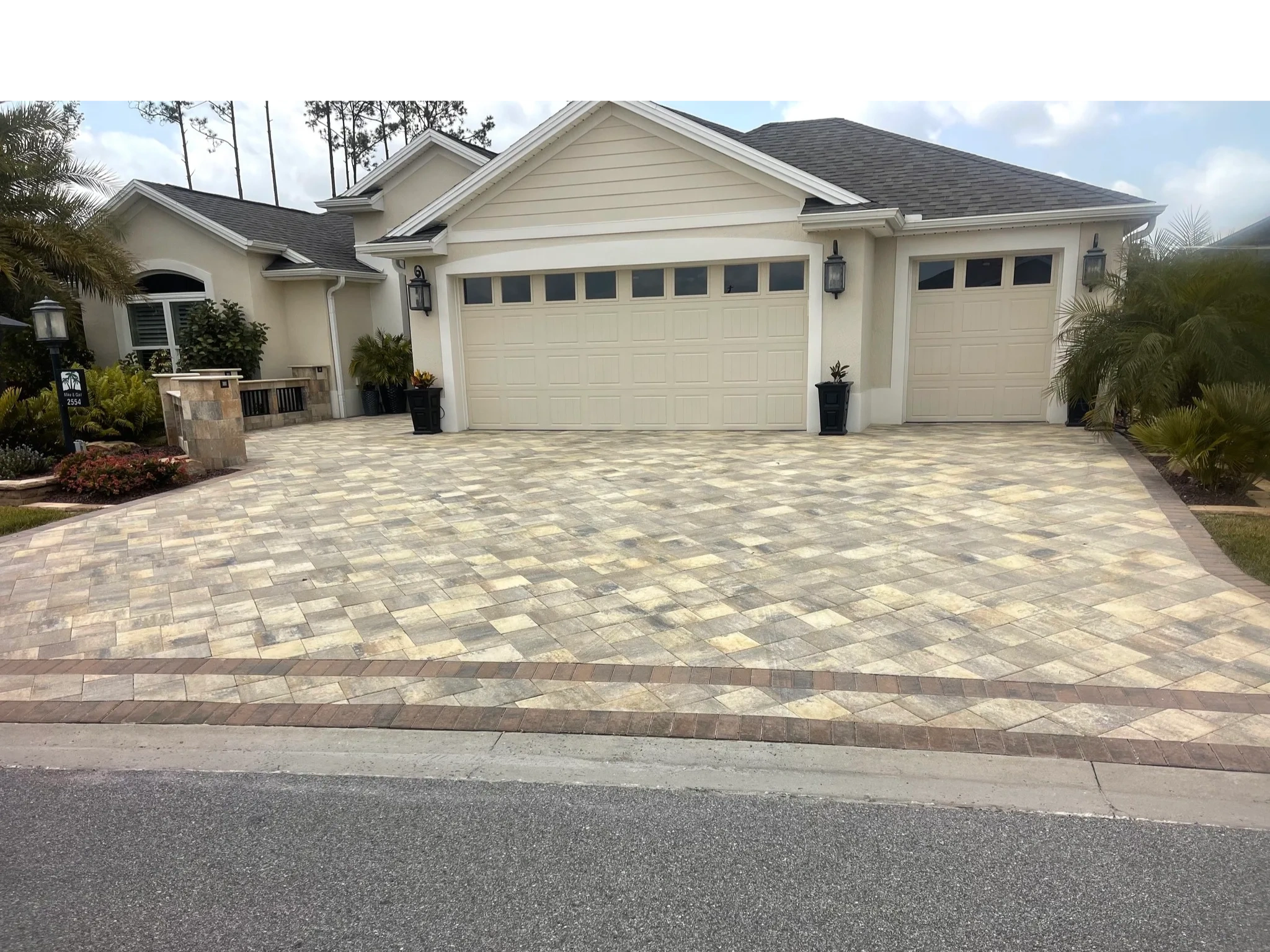 Newly paved driveway with beige and brown stone tiles in front of a modern house.