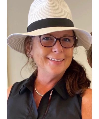 Smiling woman wearing glasses and a white hat with a black band.
