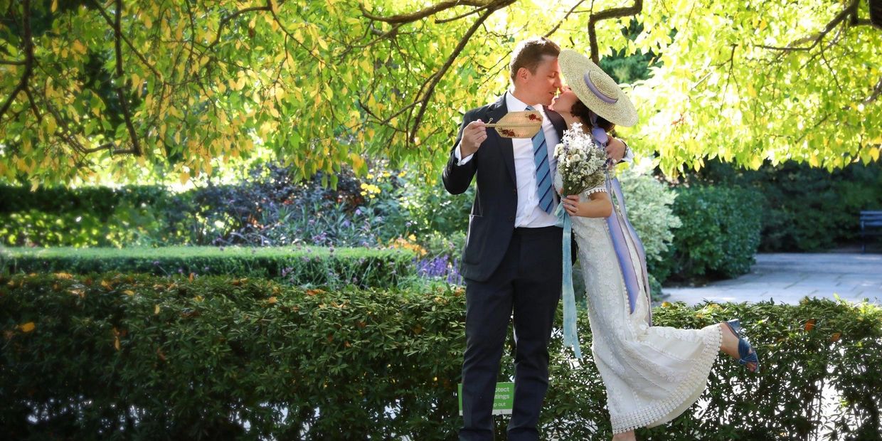 A couple kissing under a tree in a garden.
