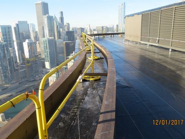 Rooftop view with yellow safety railings and city skyline in the background.