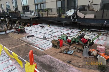 Construction site with machinery and tools laid out on insulation sheets near a building.