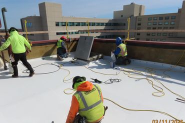 Workers installing a white roof membrane on a building rooftop.