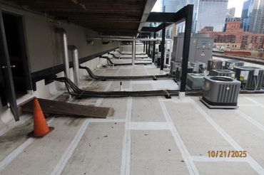 Rooftop with HVAC units, pipes, and cables under a city skyline.