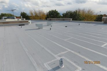 Flat commercial rooftop with vents and equipment against a cloudy sky.