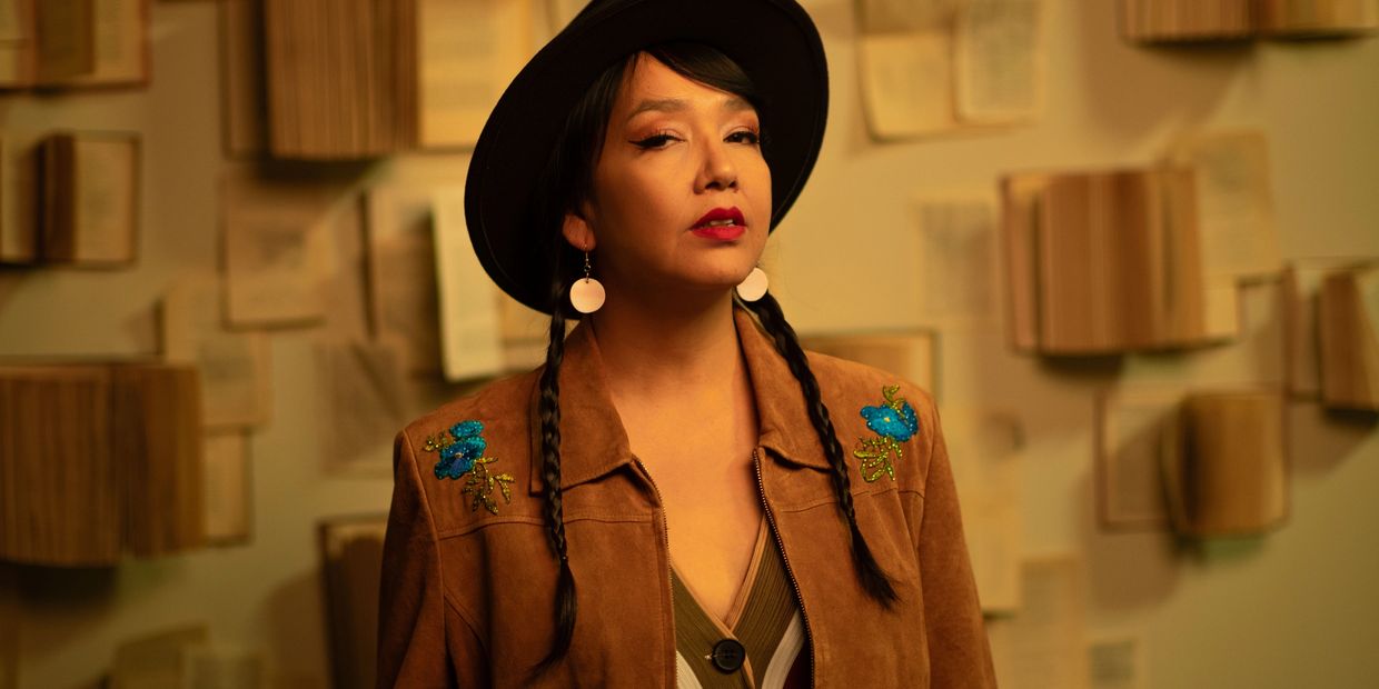Woman with braided hair and hat against a wall of open books.