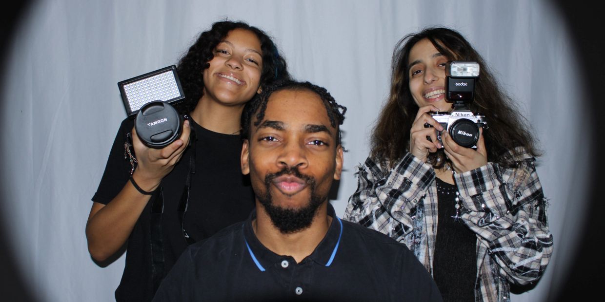 Three people smiling with cameras in hand.