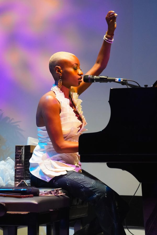 A woman passionately sings and plays piano on stage with colorful lighting.