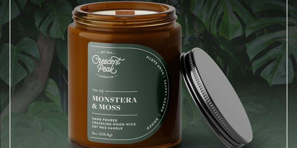 Brown jar candle labeled Monstera &amp; Moss with a black lid beside it.