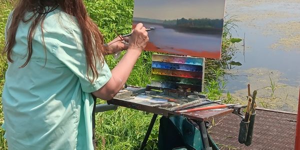 A person painting a serene river landscape outdoors.