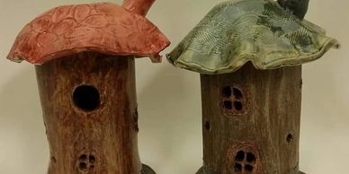 Two ceramic birdhouses shaped like tree trunks with colorful roofs.