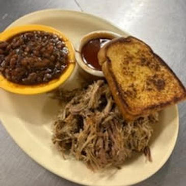 Plate of barbecue pulled pork, baked beans, Texas toast, and barbecue sauce.