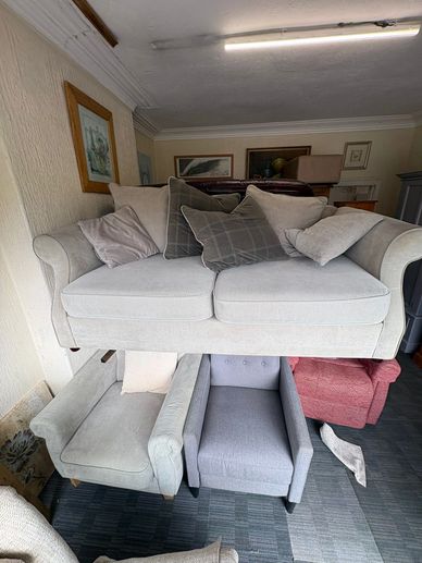 A beige sofa with cushions displayed above three armchairs in a room.