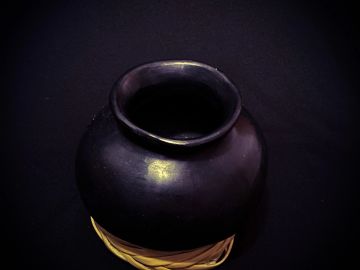 A dark, rounded clay pot on a woven base.