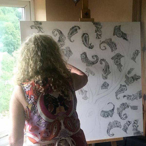Woman painting intricate patterns on a large canvas.
