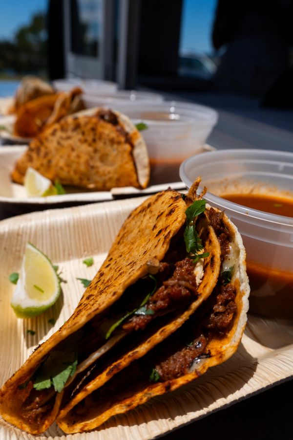 Close-up of delicious birria tacos with lime and dipping sauce on a tray.