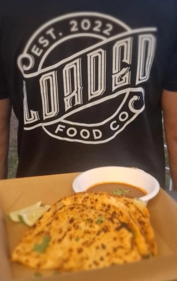 Person wearing a Loaded Food Co. shirt with food in front, including flatbread and sauce.
