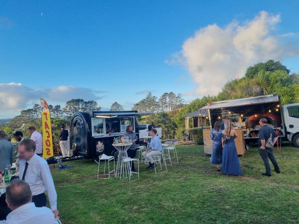 People enjoying a sunny outdoor event with food trucks and casual seating on grass.