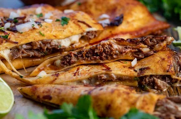 Close-up of delicious birria tacos filled with meat and cheese, garnished with onions and cilantro.
