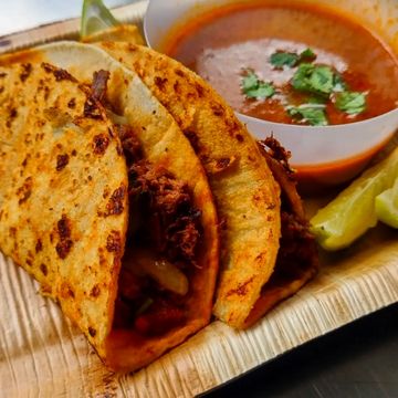 Three crispy tacos with meat and a side of salsa and lime wedges.
