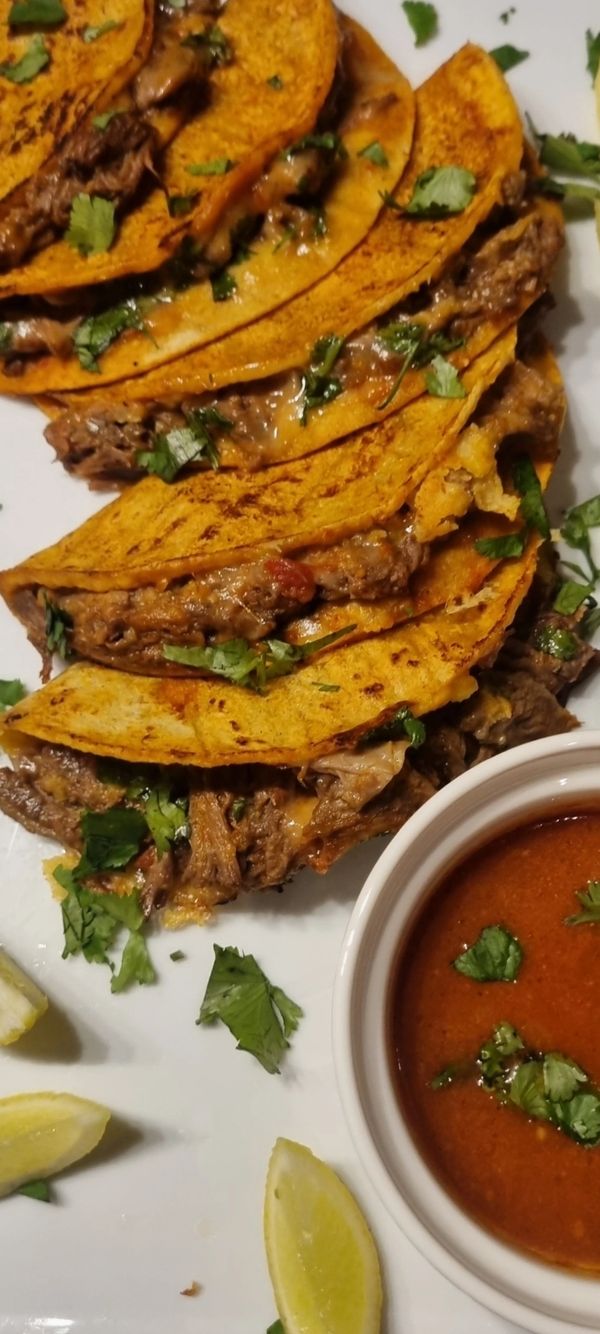 Delicious tacos with beef, cilantro, and a side of dipping sauce and lemon wedges.