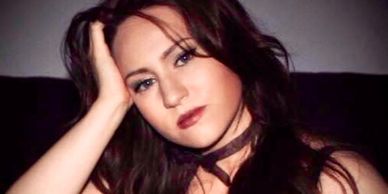 Woman with dark hair resting her head on her hand, looking thoughtfully.