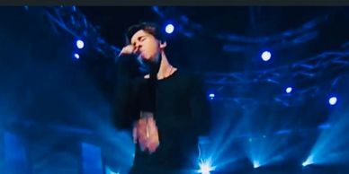 A male singer passionately performing on stage with blue lighting.