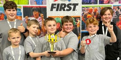 Young boys proudly holding a trophy at a FIRST robotics event.