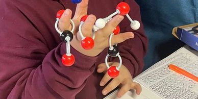 Person holding molecular models over a periodic table.