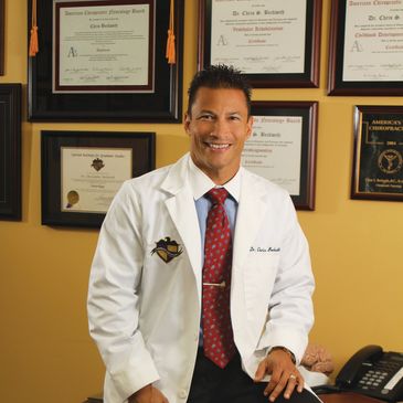 Dr. Chris Beckwith is smiling in a white coat. Behind him are framed certifications.