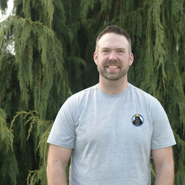 White male, Olan, owner of company smiling with green trees behind.