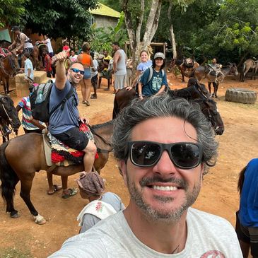 White man smiling with sunglasses in front, white man with sunglasses smiling in background on horse