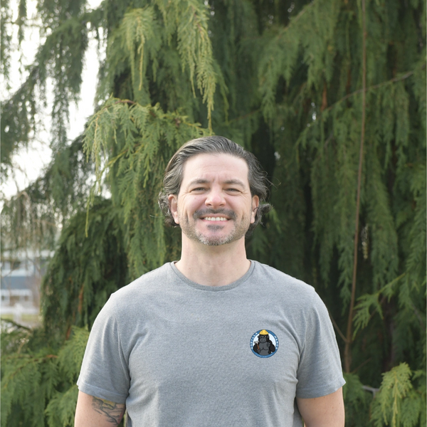 White male, Mark, owner of company smiling with green trees behind.