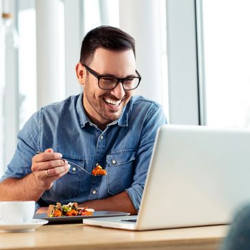 Man enjoying a meal while watching something on his laptop with a smile.