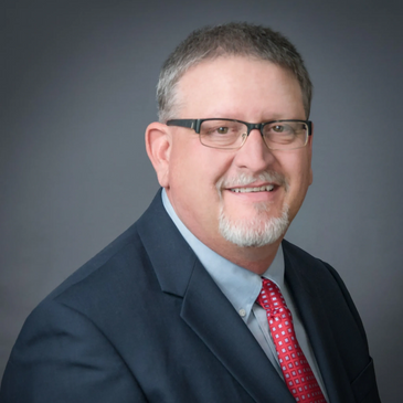 Professional man with glasses, suit, and red tie smiling.
