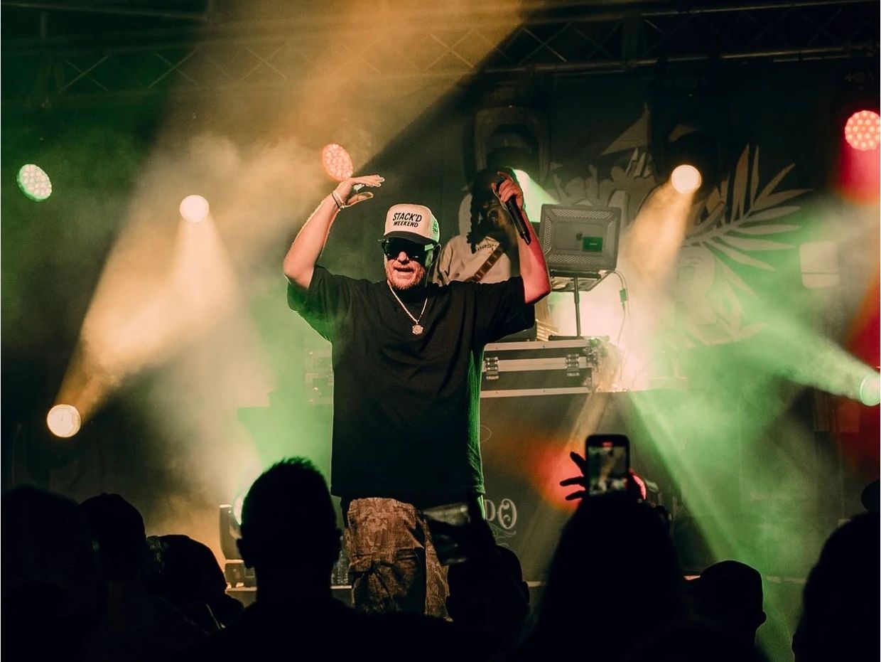 Man with mic performs on stage with colorful lights and audience silhouettes.