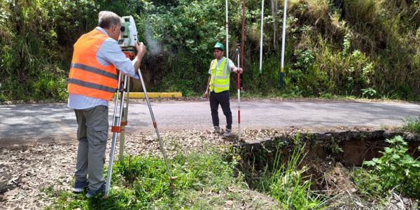 Two surveyors measuring land near a road with safety vests and equipment.
