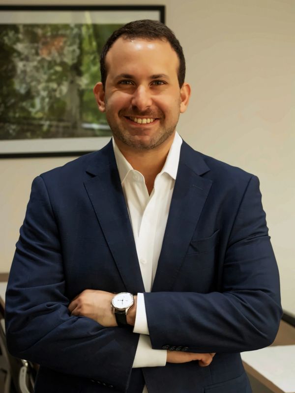 Homem sorridente vestindo terno azul escuro e camisa branca.