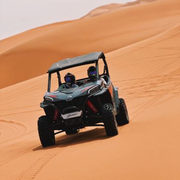 Two people riding a dune buggy on sand dunes.