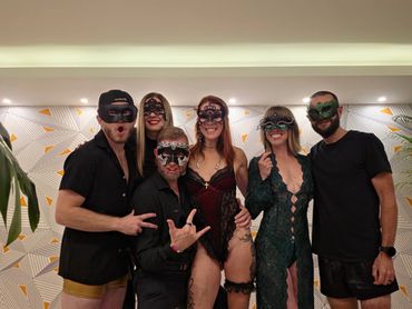 Group of six friends wearing masks and party outfits indoors.