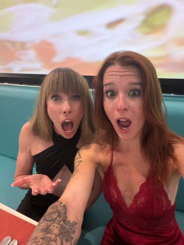 Two women in elegant dresses making surprised expressions while taking a selfie.