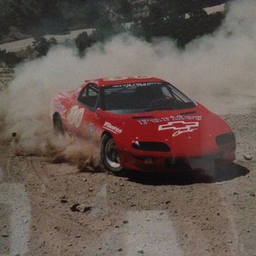 Red race car kicking up dust while drifting on a dirt track.