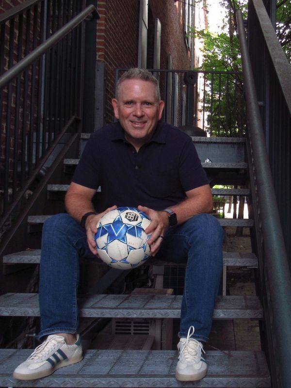 Man sitting on stairs holding a soccer ball.