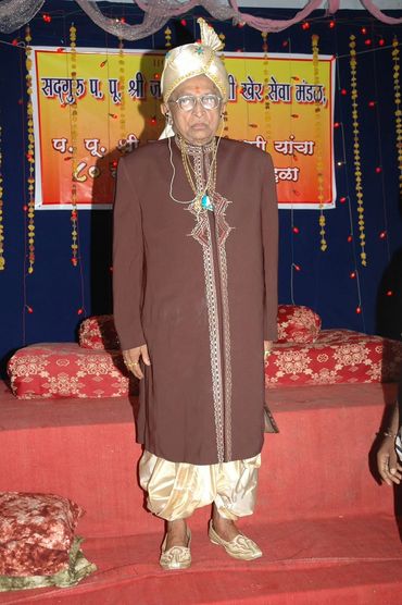 Elderly man in traditional Indian attire at a decorated event stage.