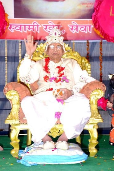 Elderly man in traditional attire sitting on a decorated throne.