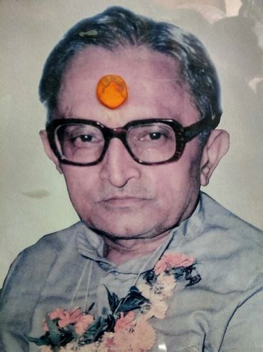 Portrait of an elderly man with a tilak on forehead and flower garland.