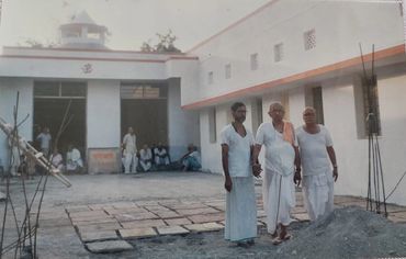 Three men in traditional white attire standing outside a building.
