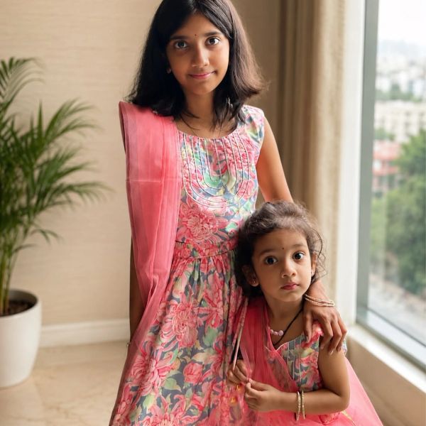 Two sisters in matching floral dresses indoors.