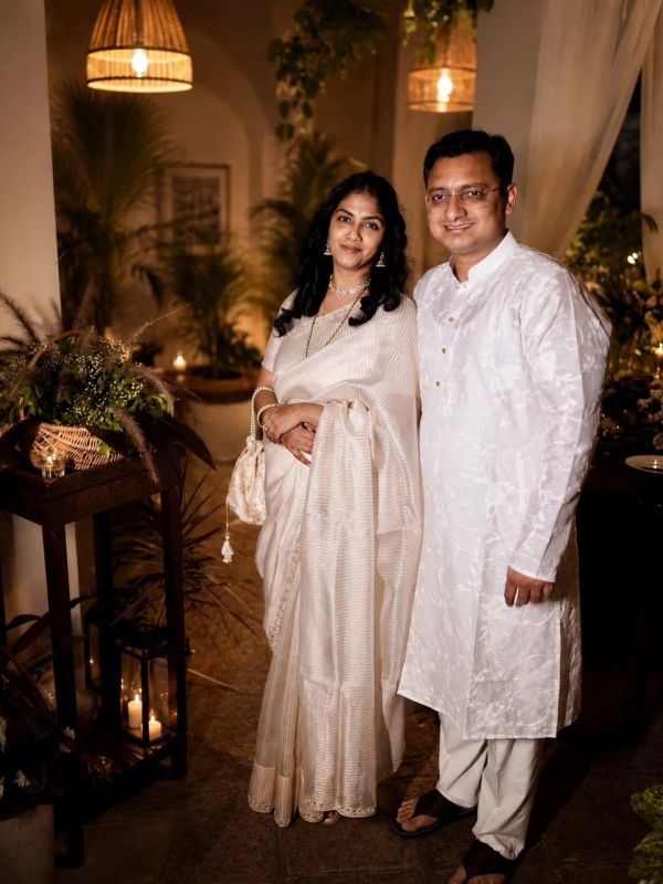 A couple dressed in traditional white attire, smiling indoors.